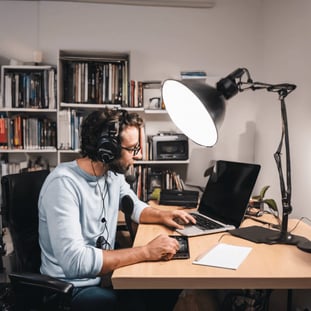 Image réaliste d'un homme qui écoute un podcast assis sur son bureau.